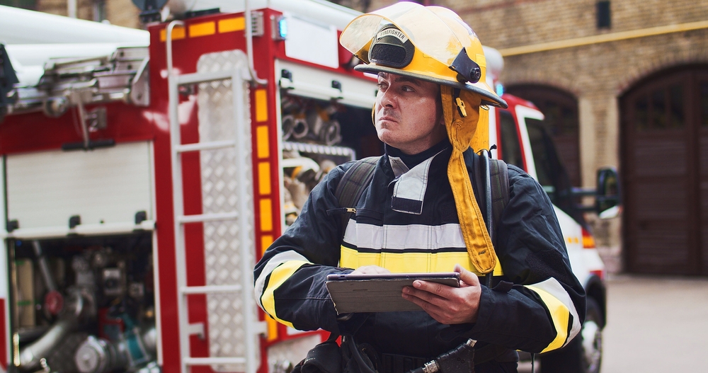 Portrait of fireman in helmet and gull equipment viewing on sides and writting data to tablet.